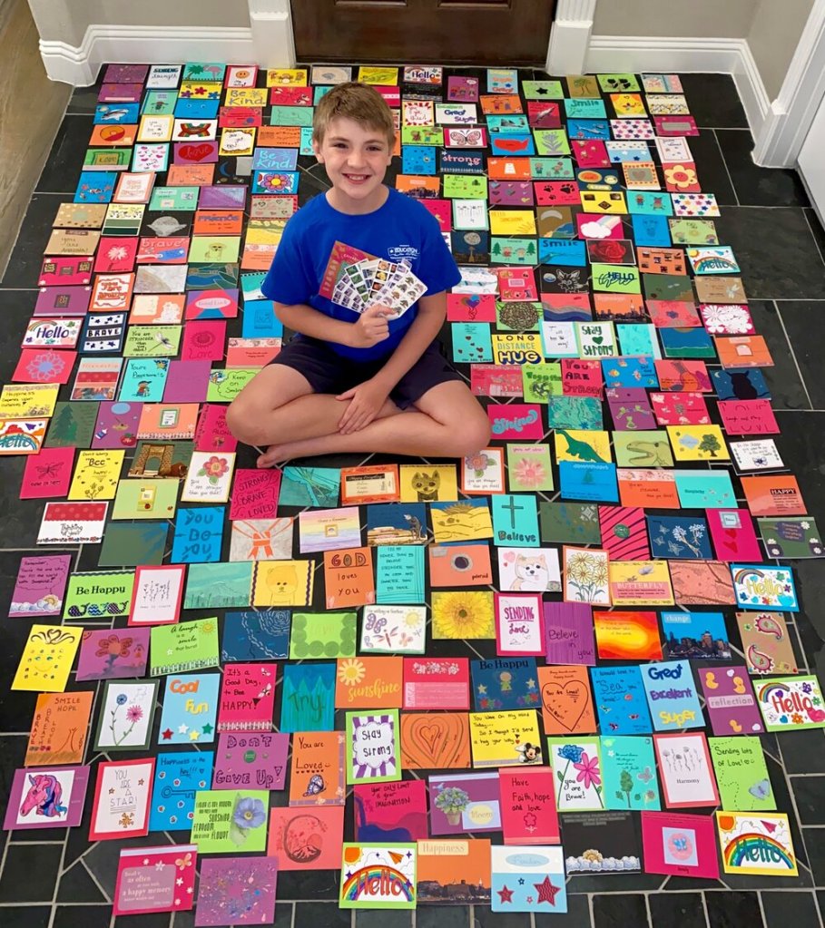 A young boy surrounded by dozens of decorated notecards on the floor
