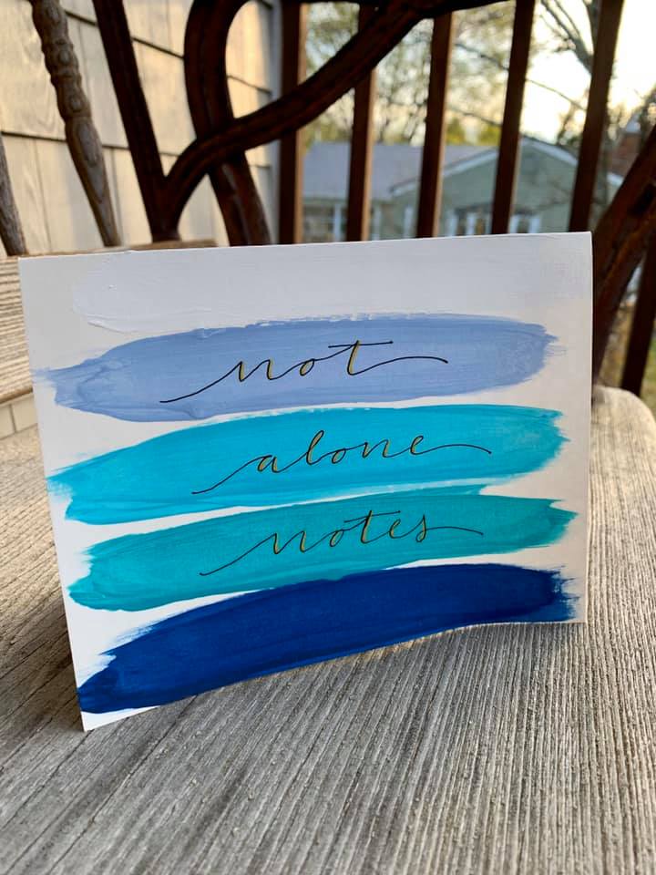 Photo of a white and blue notecard that reads "not alone notes" on the front in cursive.