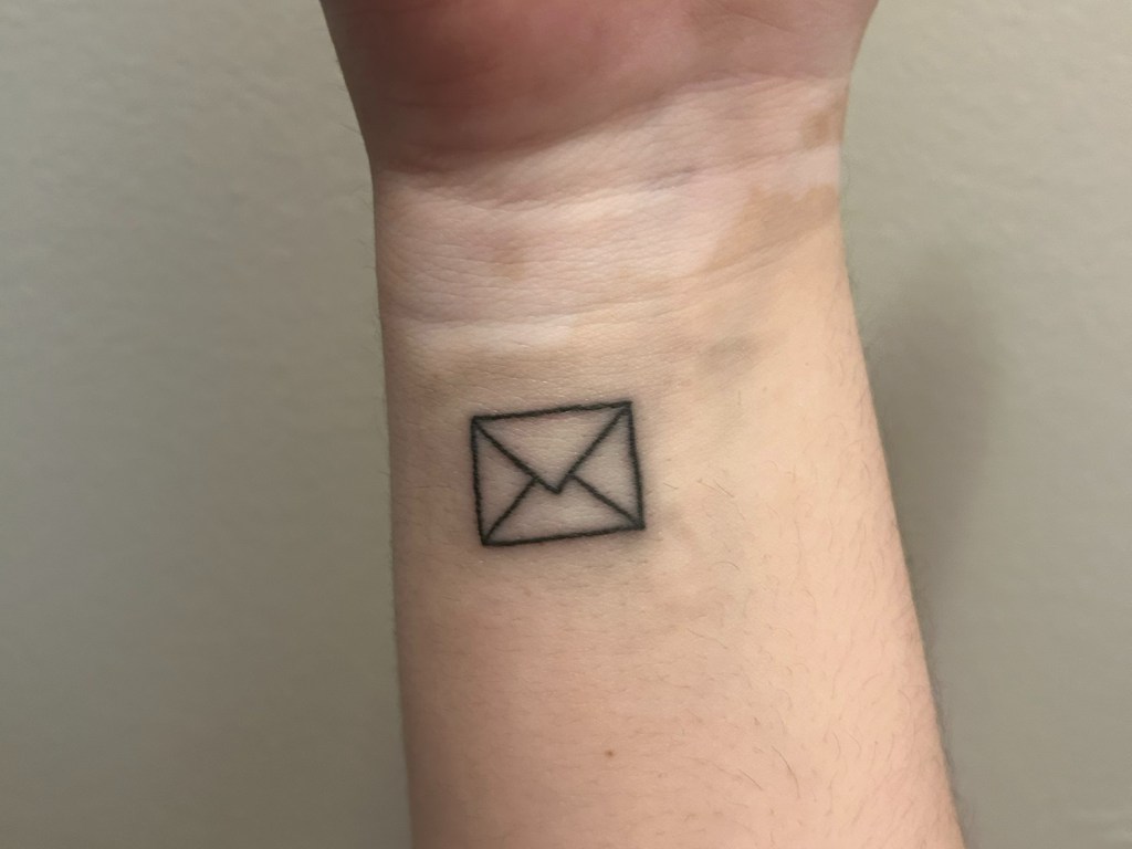 a wrist with a simple envelope outline tattoo